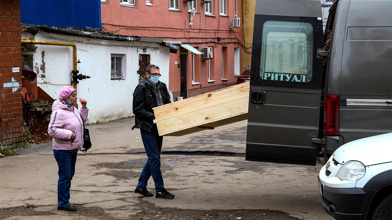
					A wooden coffin is placed into a hearse.					 					Roman Yarovitcyn / AP / TASS				