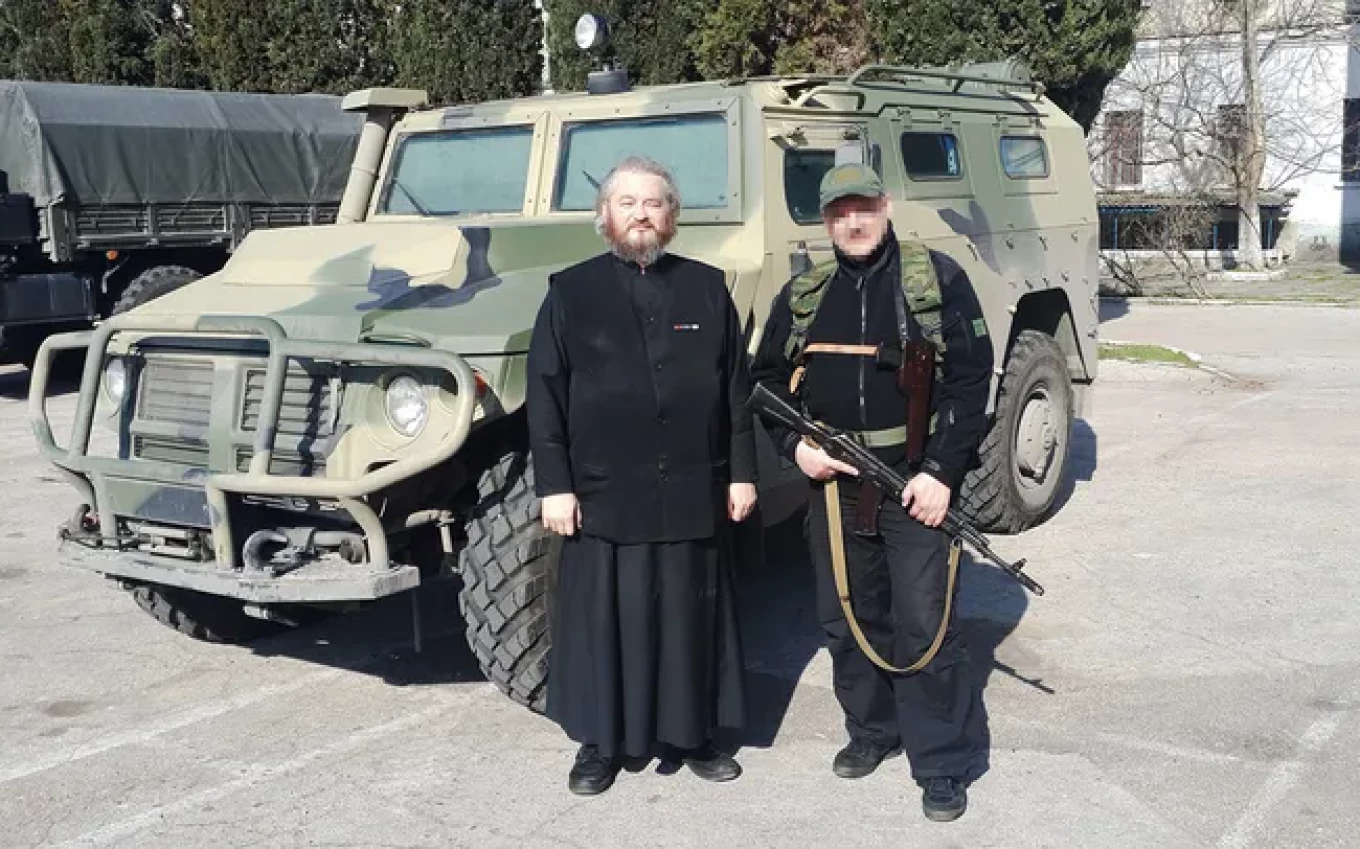 
					Father Dimitry Vasilenkov and an unmarked soldier stand in front of a Russian Tigr armored car, March 2014.					 					Dimitri Vasilenkov / VKontakte				