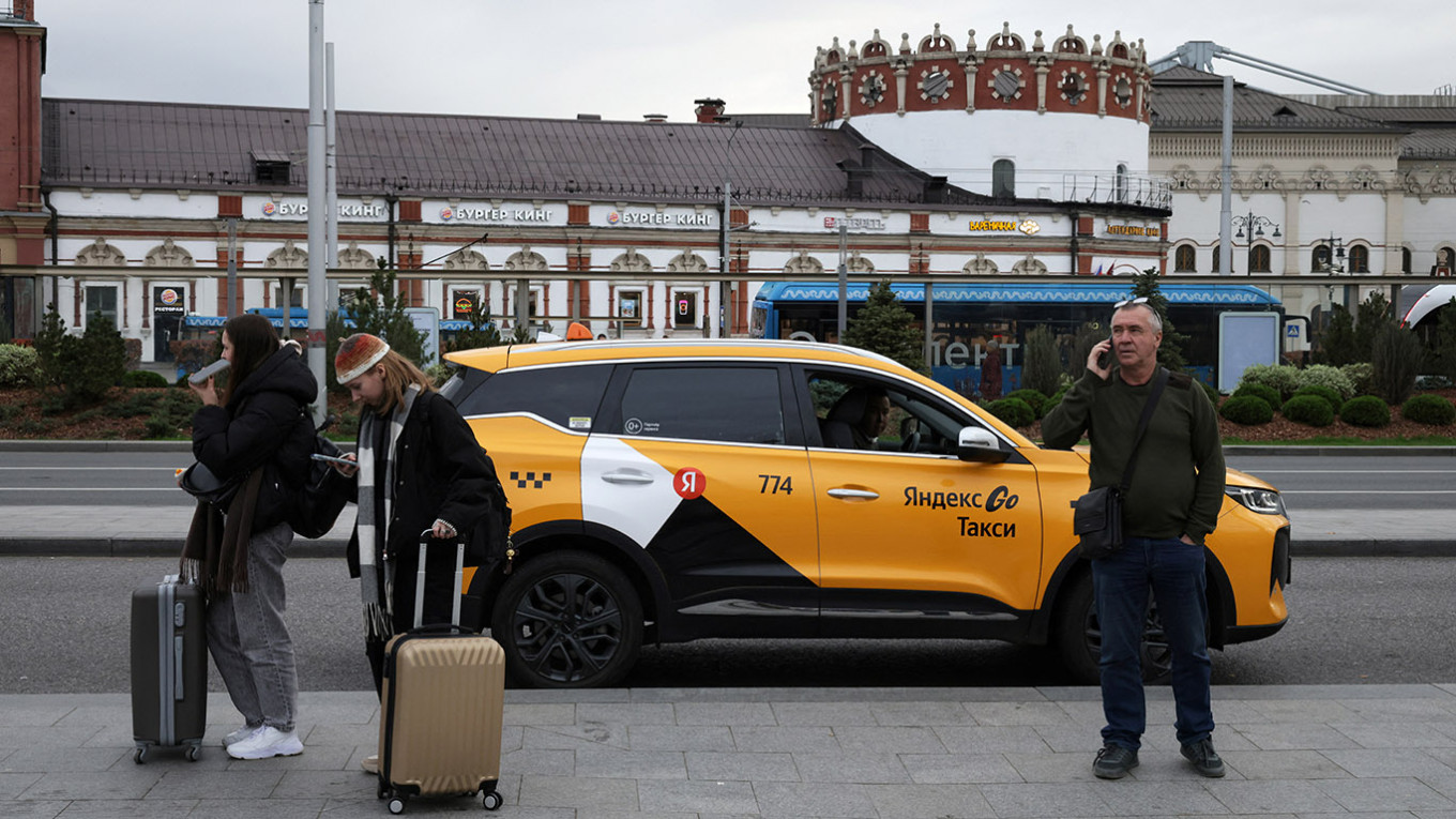 
					People stand next to a Yandex Taxi car on a street in Moscow.					 					REUTERS / Anastasia Barashkova				