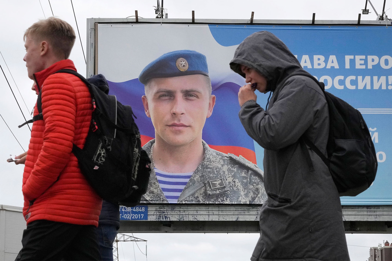 Двое молодых людей проходят мимо рекламного щита в Сент-Луисе.  Петербург с фотографией русского офицера.  Дмитрий Ловецкий / AP / ТАСС