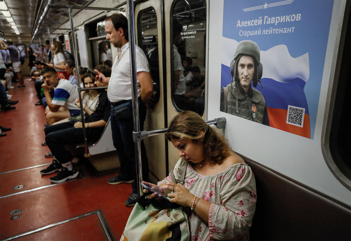 
					A woman sits in a Moscow subway car near a poster showing a Russian soldier.					 					Yuri Kochetkov / EPA / TASS				