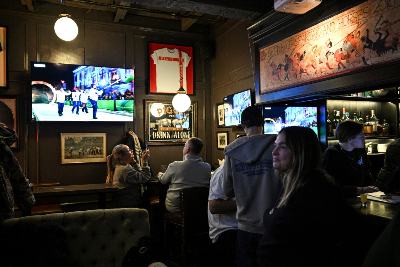 
					People watch the live TV broadcast of the Milano Cortina 2026 Winter Olympic Games opening ceremony at a bar in central Moscow, on Feb. 6. 					 					Hector Retamal / AFP				