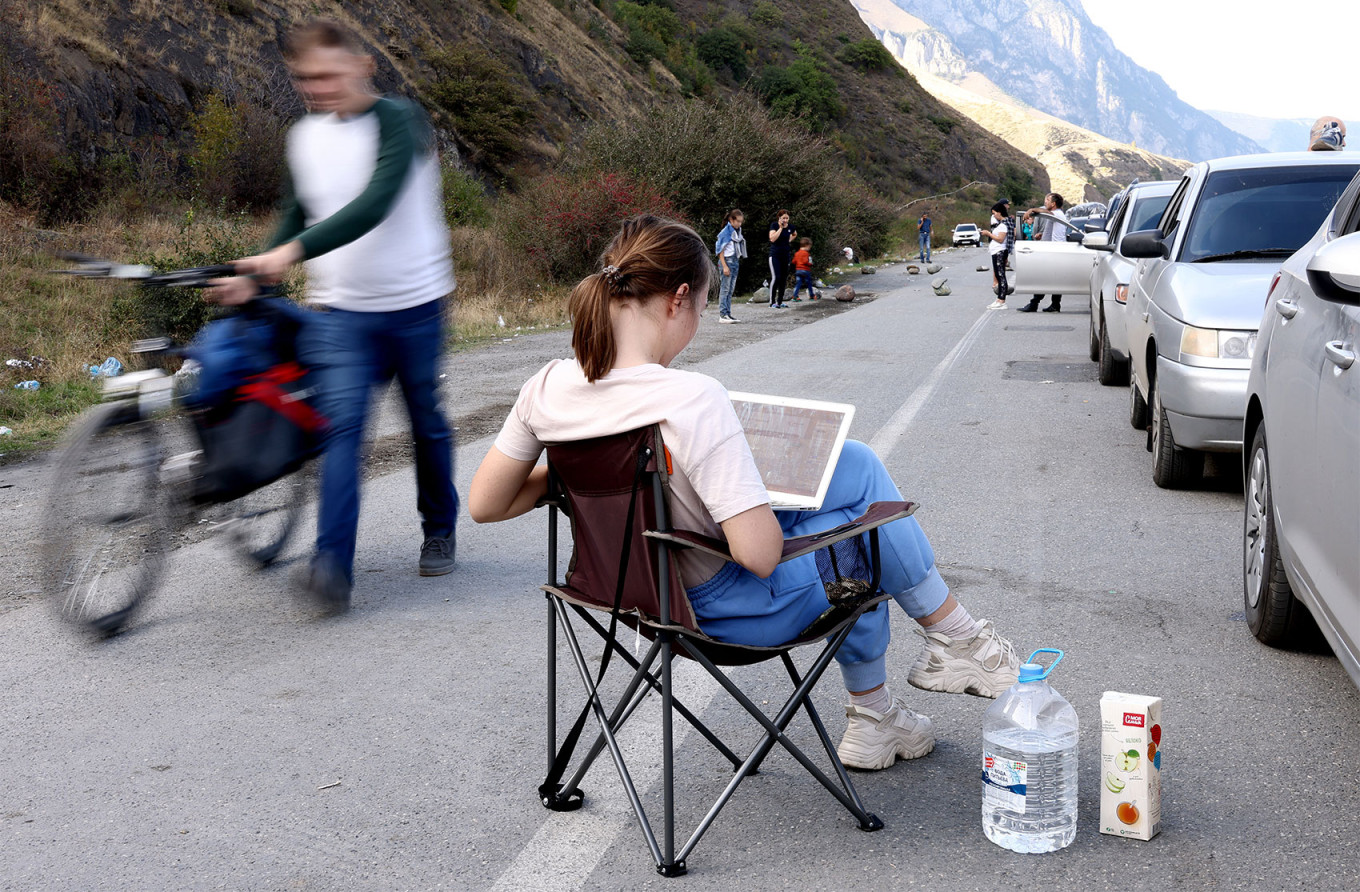 
					A woman on her laptop by a line of vehicles at the Russian-Georgian border, September 2022. 					 					Valery Sharifulin / TASS				