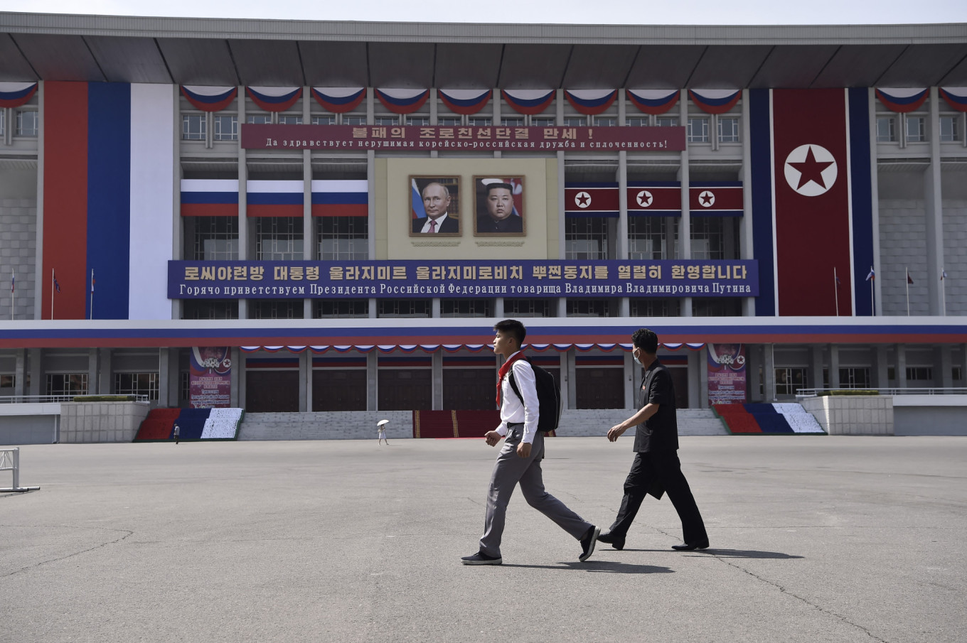 People walk past portraits of Russian President Vladimir Putin (L) and North Korea's leader Kim Jong Un with banners that translate as "Long live the undefeated friendship and unity of DPRK-Russia!" and "We warmly welcome Comrade Vladimir Vladimirovich Putin, the President of the Russian Federation", outside the Pyongyang Indoor Stadium in Pyongyang, June 2024.